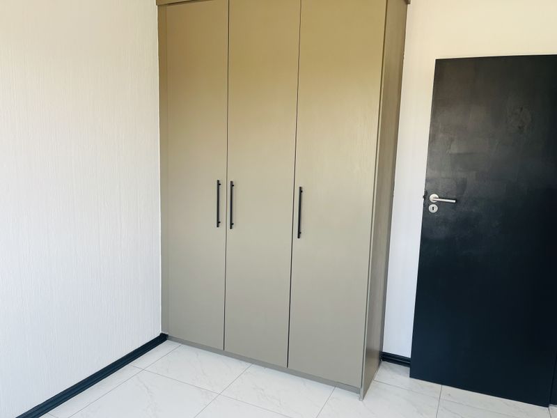 A clean bedroom interior featuring a modern built-in wardrobe, white tiled flooring, and a contrasting black internal door.