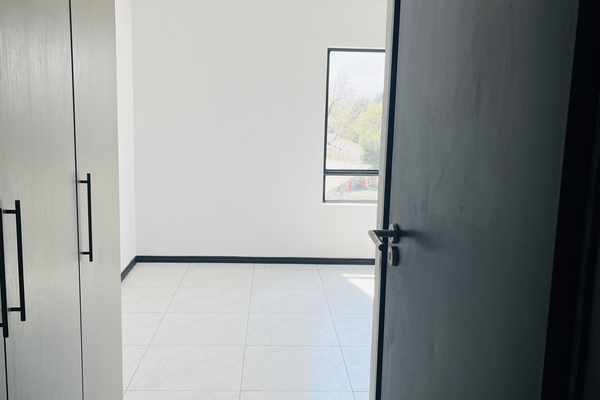 A bright, empty bedroom featuring modern tiled flooring, built-in cupboards, and contemporary track lighting, offering a clean and neutral living space.