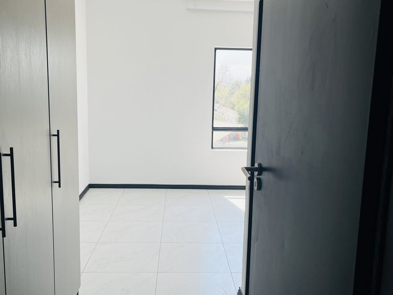 A bright, empty bedroom featuring modern tiled flooring, built-in cupboards, and contemporary track lighting, offering a clean and neutral living space.