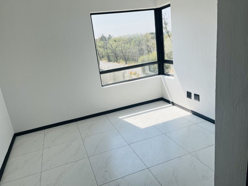 A bright, empty bedroom featuring modern marble-look floor tiles, black skirting boards, and a large corner window with natural light.
