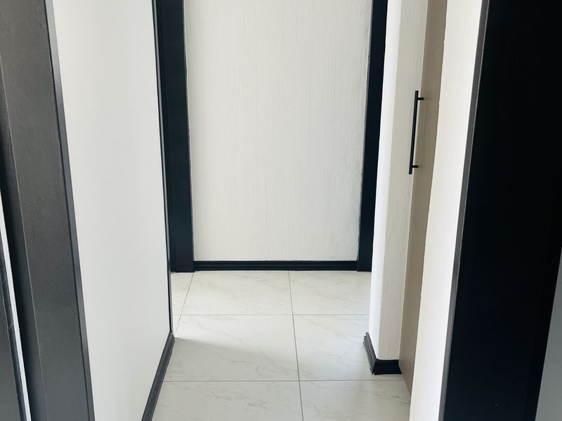 A clean, modern hallway featuring white marble-look floor tiles, contrasting black door frames, and black skirting boards with a built-in storage cupboard.