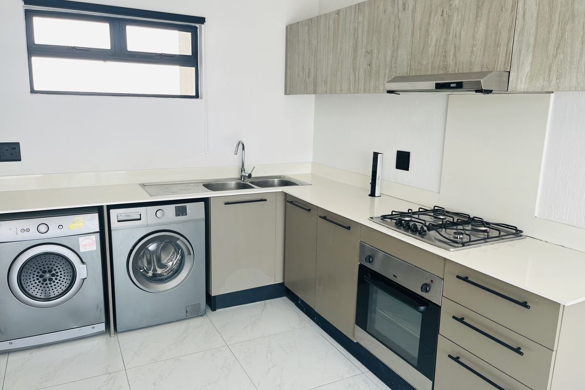 Modern kitchen featuring sleek cabinetry, stone countertops, gas hob, built-in oven, extractor fan, and integrated space for laundry appliances.