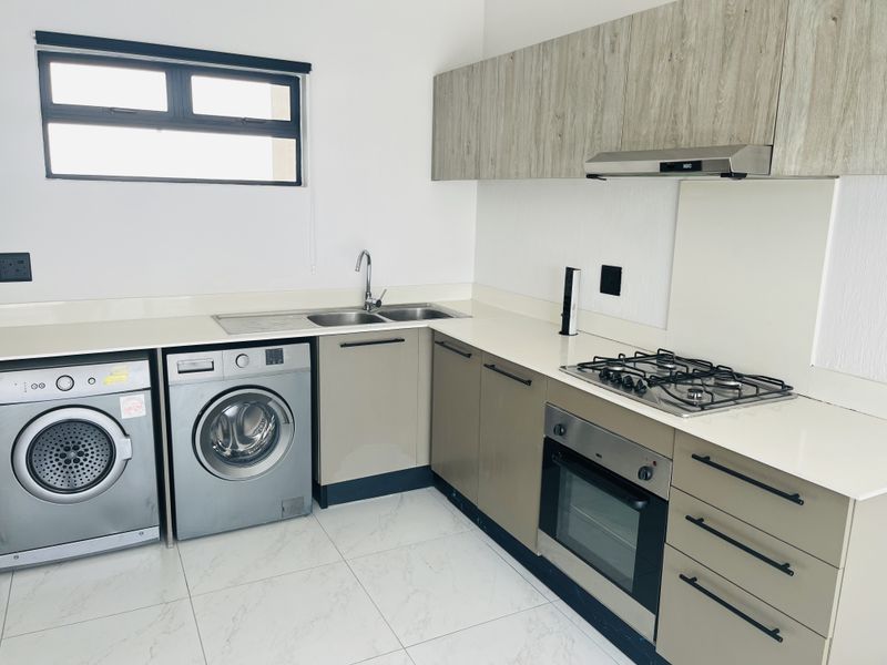 Modern kitchen featuring sleek cabinetry, stone countertops, gas hob, built-in oven, extractor fan, and integrated space for laundry appliances.
