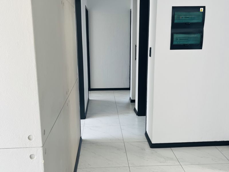 A clean, modern hallway featuring white marble-look floor tiles, black trim accents, and a built-in electrical distribution board.
