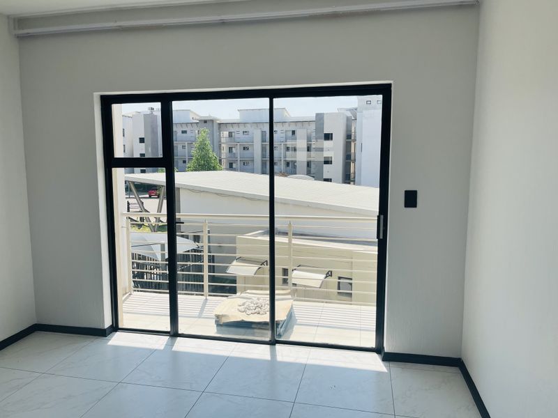 An empty living room featuring modern tiled flooring and a large sliding glass door that opens onto a private balcony.