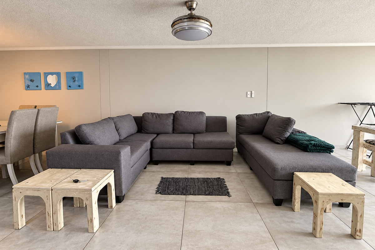 A spacious living area featuring neutral tiled flooring, a central ceiling fan, and a clean, minimalist wall finish.