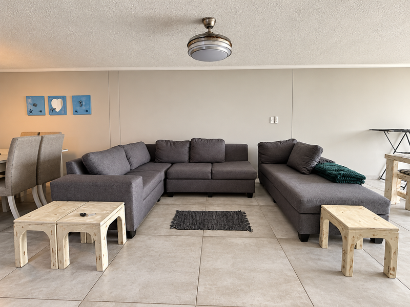 A spacious living area featuring neutral tiled flooring, a central ceiling fan, and a clean, minimalist wall finish.
