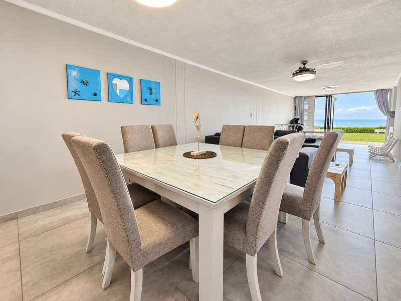 Open plan living and dining area featuring neutral tiled flooring, ceiling fans, and large sliding glass doors leading to an outdoor patio with ocean views.