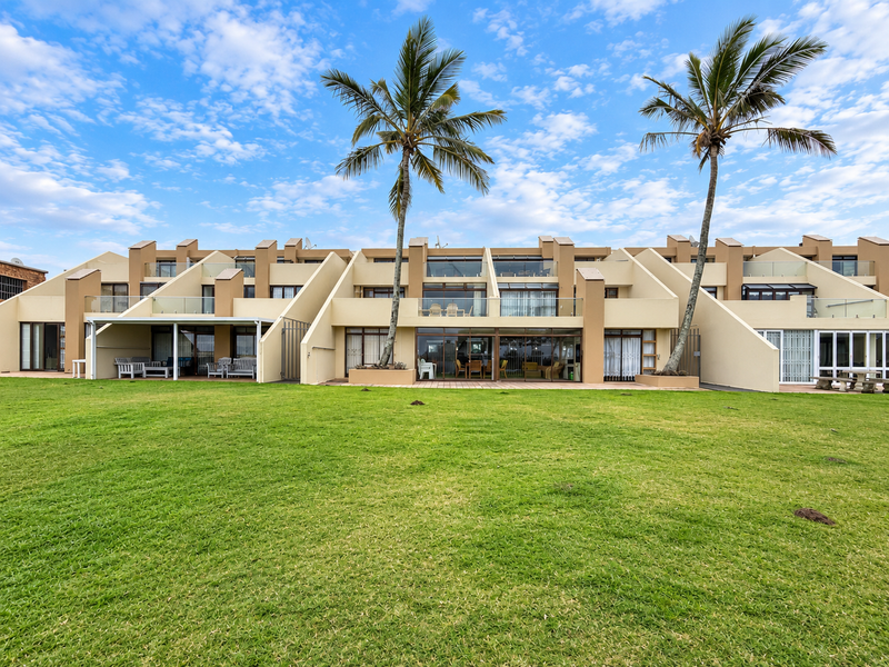 Rear view of a multi-unit apartment complex featuring private ground-floor patios, glass balcony railings, and a well-maintained communal lawn area.