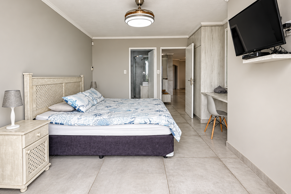 Spacious bedroom featuring neutral tiled flooring, built-in cupboards, a dedicated desk area, and direct access to an en-suite bathroom.