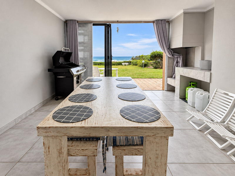 Covered patio area featuring a built-in braai, tiled flooring, and large stacking doors opening to a garden with ocean views.