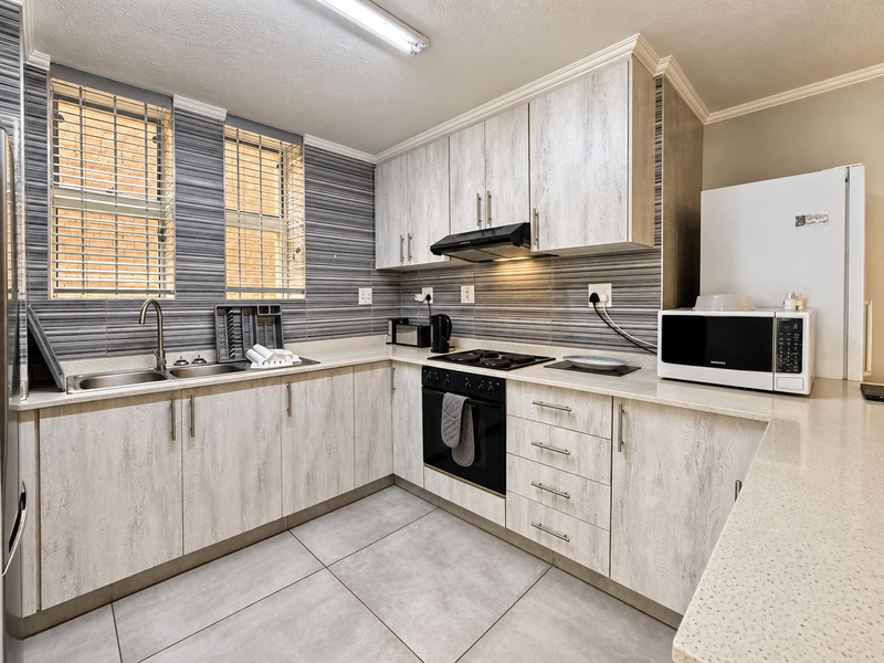 Modern kitchen featuring light wood-grain cabinetry, stone countertops, integrated oven and hob, and a stylish tiled backsplash with ample natural light.