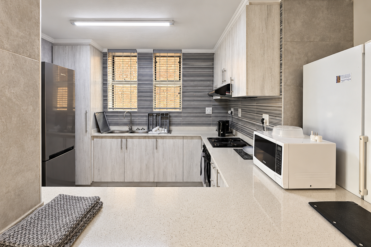 A modern, well-maintained kitchen featuring light wood-grain cabinetry, stone countertops, a tiled backsplash, and integrated cooking appliances.
