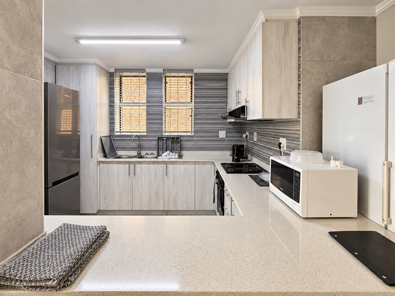 A modern, well-maintained kitchen featuring light wood-grain cabinetry, stone countertops, a tiled backsplash, and integrated cooking appliances.