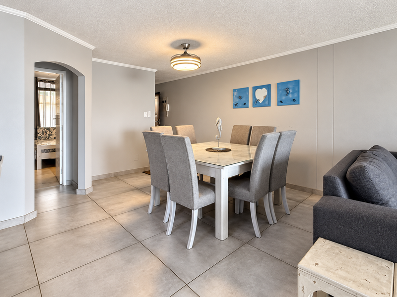 Open plan living and dining area featuring neutral ceramic floor tiles, coved ceilings, and a central ceiling fan, with an arched doorway leading to a bedroom.