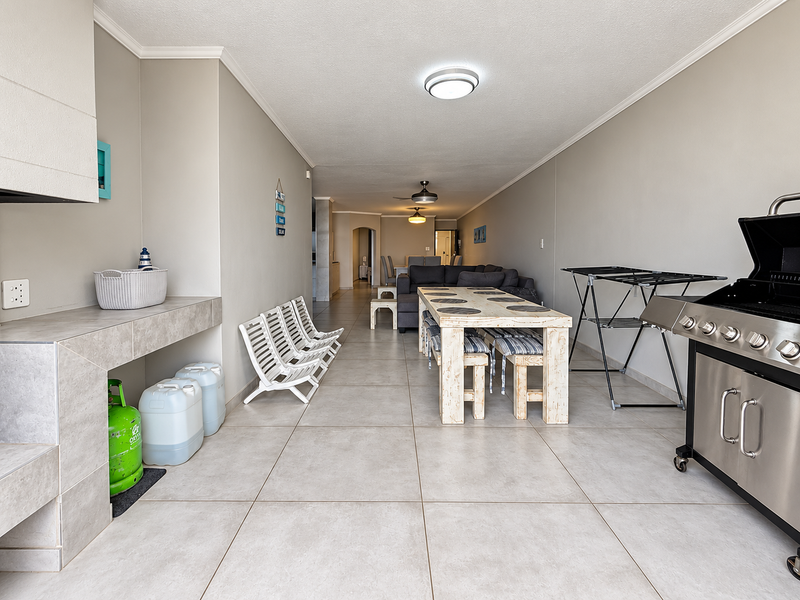 Spacious covered patio featuring tiled flooring, a built-in braai area, and ceiling fan, providing a functional outdoor entertainment space.