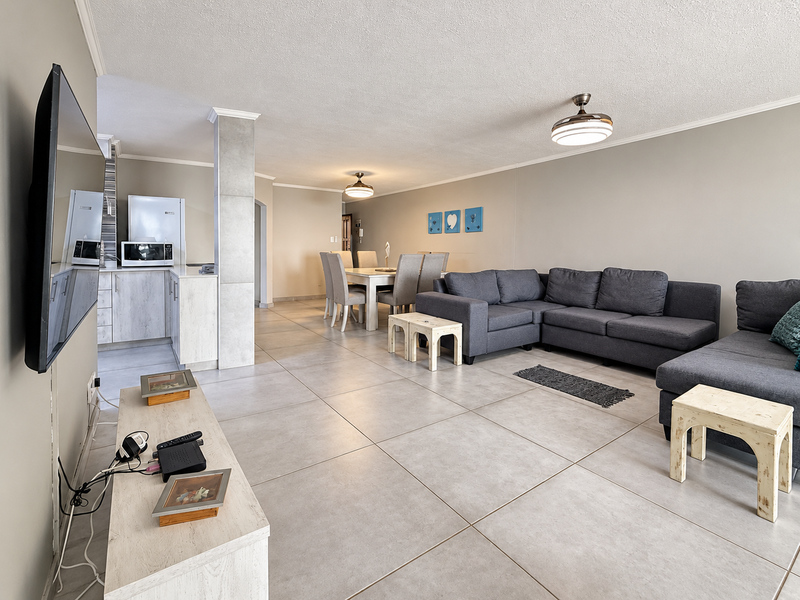 Spacious open-plan living and dining area featuring large format floor tiles, neutral wall tones, and an integrated kitchen with modern cabinetry.