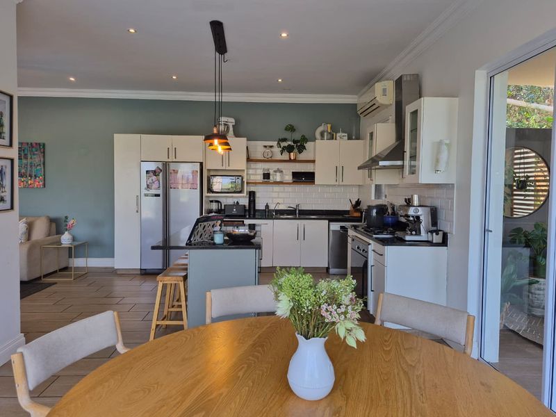 Open-plan kitchen and dining area featuring modern cabinetry, subway tile backsplash, a central island, and direct access to an outdoor patio space.