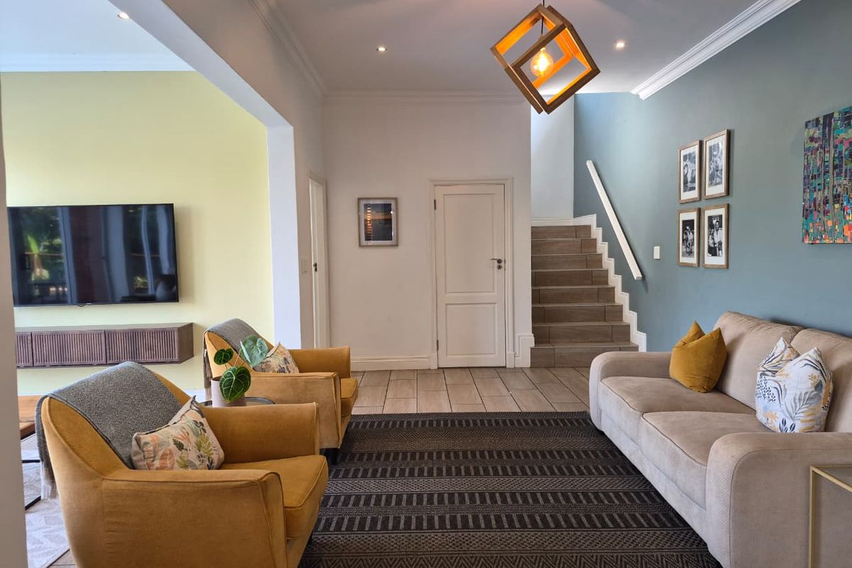 A well-maintained living room featuring tiled flooring, a staircase with a handrail, recessed lighting, and a wall-mounted media console.