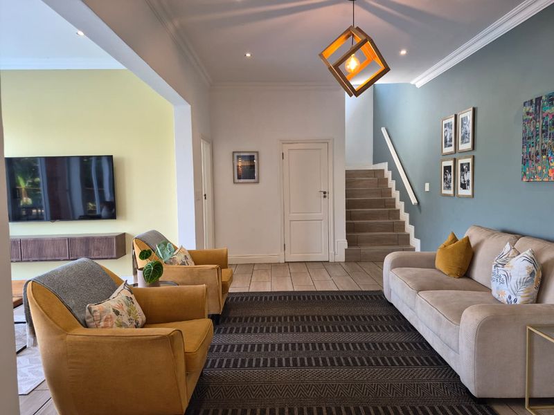 A well-maintained living room featuring tiled flooring, a staircase with a handrail, recessed lighting, and a wall-mounted media console.