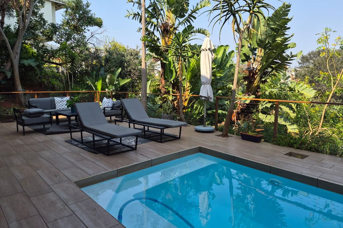 Outdoor pool area featuring a tiled deck, wire balustrade with timber handrail, and lush garden surroundings.