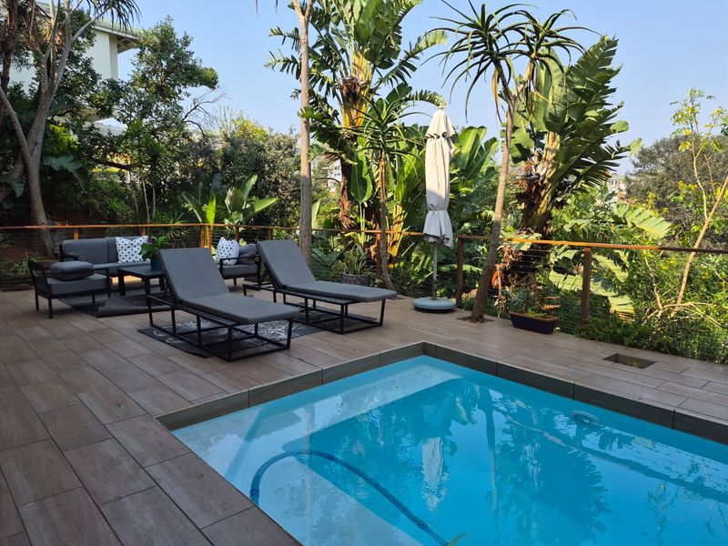 Outdoor pool area featuring a tiled deck, wire balustrade with timber handrail, and lush garden surroundings.