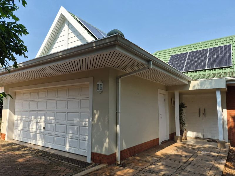 Front elevation of the townhouse featuring a garage, paved driveway, and roof-mounted solar panels.