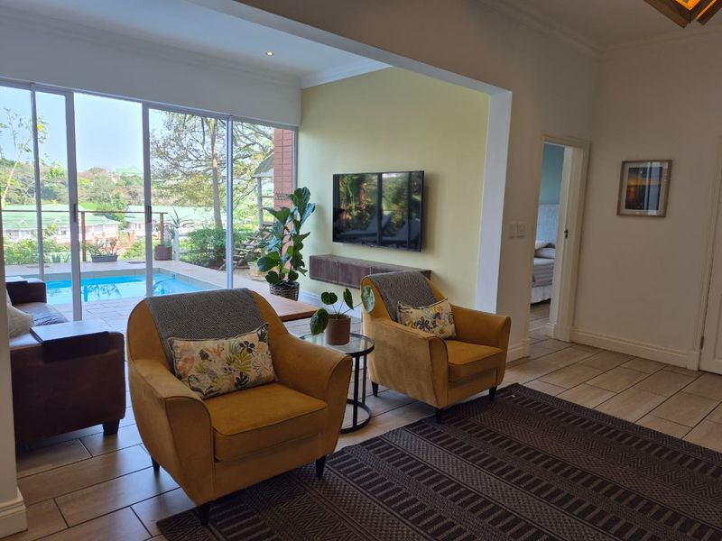 Spacious living room featuring large sliding glass doors that open to a pool area, tiled flooring, and a wall-mounted television with a floating console.