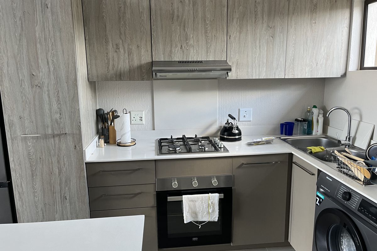 Modern kitchen featuring wood-grain cabinetry, stone countertops, a gas hob with extractor fan, built-in oven, and an integrated washing machine.