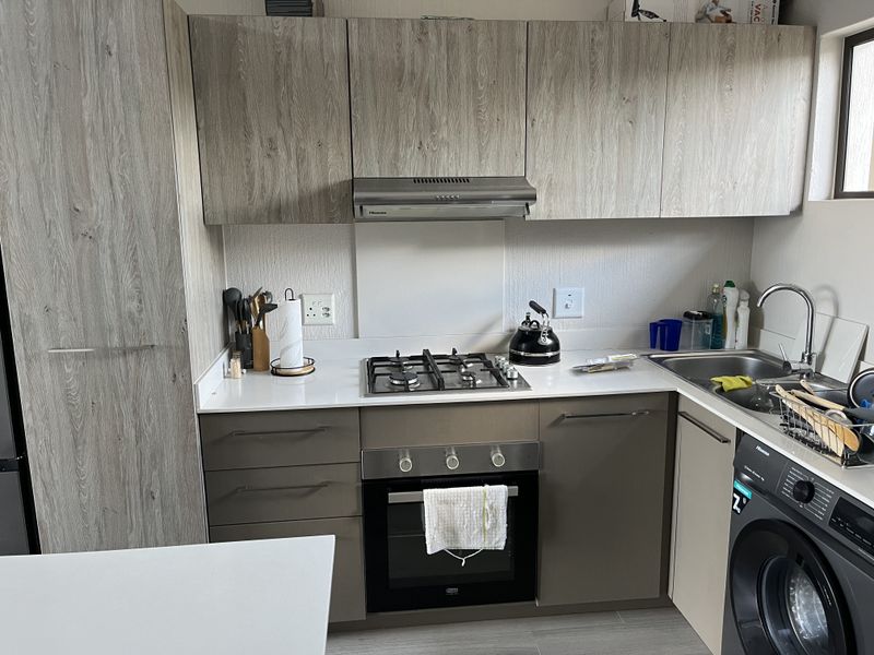 Modern kitchen featuring wood-grain cabinetry, stone countertops, a gas hob with extractor fan, built-in oven, and an integrated washing machine.