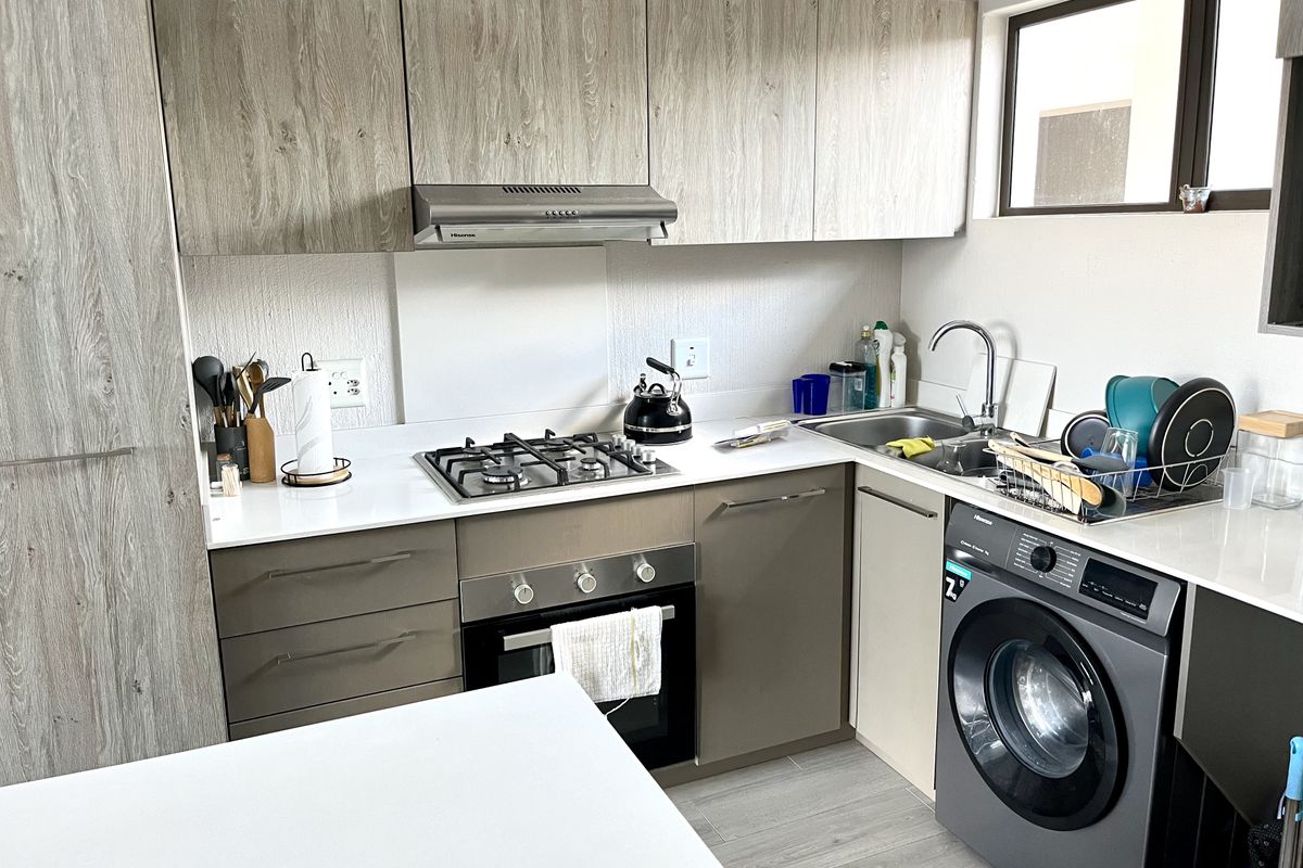 Modern kitchen featuring wood-grain cabinetry, quartz countertops, a gas hob, built-in oven, extractor fan, and an integrated washing machine.