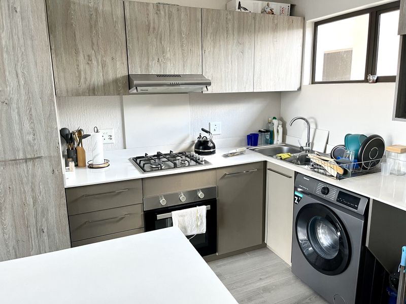 Modern kitchen featuring wood-grain cabinetry, quartz countertops, a gas hob, built-in oven, extractor fan, and an integrated washing machine.