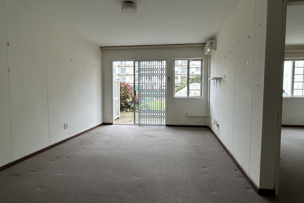 An empty living room featuring carpet flooring, a split system air conditioner, and a sliding glass door with a security gate leading to the garden.
