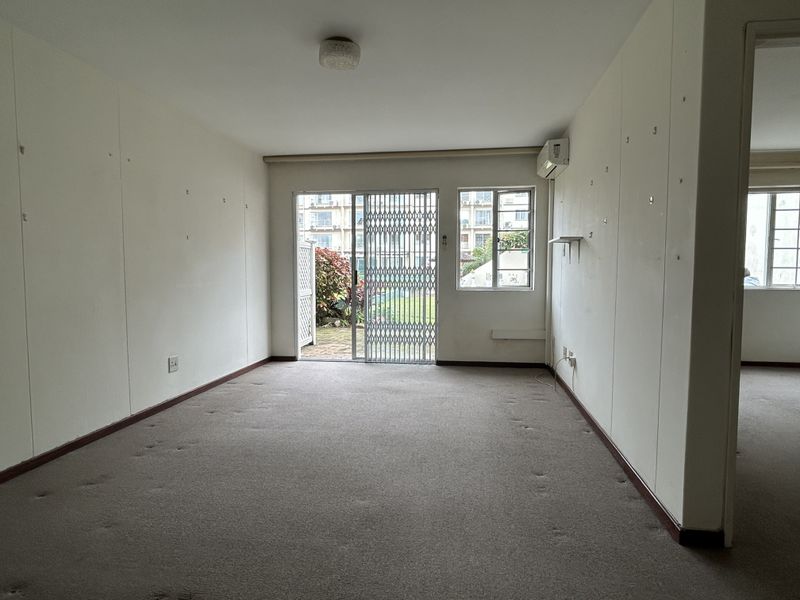 An empty living room featuring carpet flooring, a split system air conditioner, and a sliding glass door with a security gate leading to the garden.