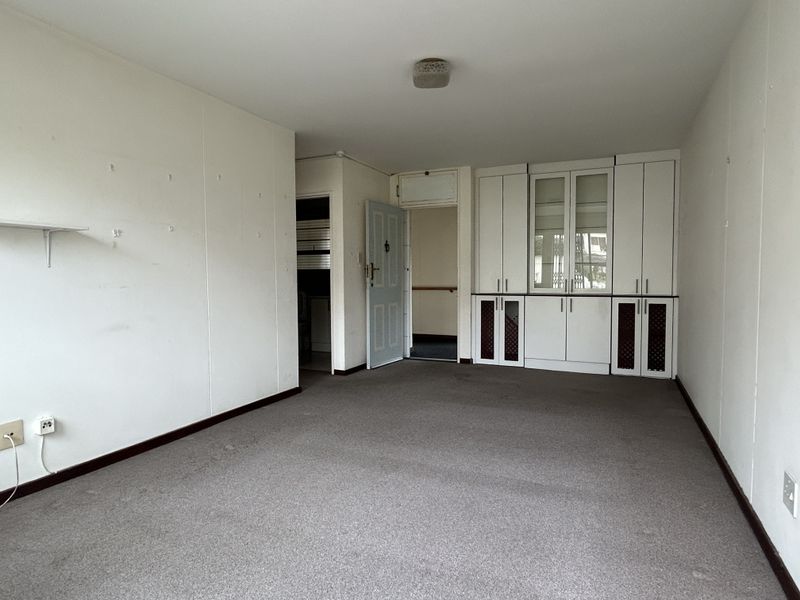 An empty living room featuring built-in storage cabinetry, neutral carpeting, and access to adjacent rooms.