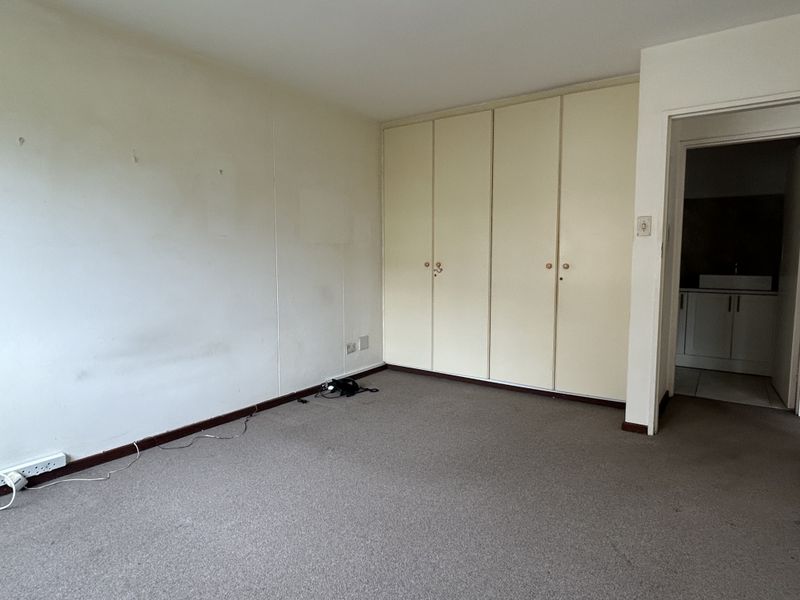 An empty bedroom featuring built-in cupboards and carpeted flooring, requiring cosmetic updates to the walls and finishes.