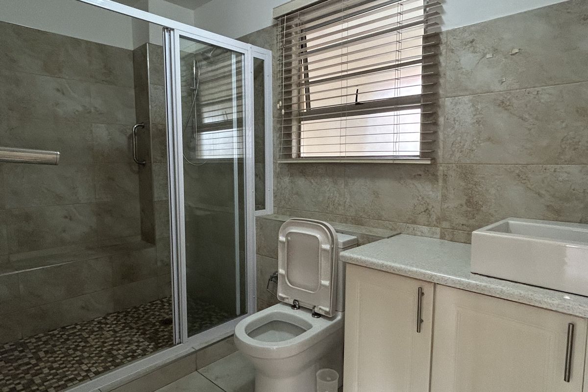 A functional bathroom featuring a walk-in shower with glass enclosure, a vanity with a vessel sink, and neutral wall tiling.