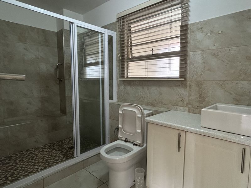 A functional bathroom featuring a walk-in shower with glass enclosure, a vanity with a vessel sink, and neutral wall tiling.