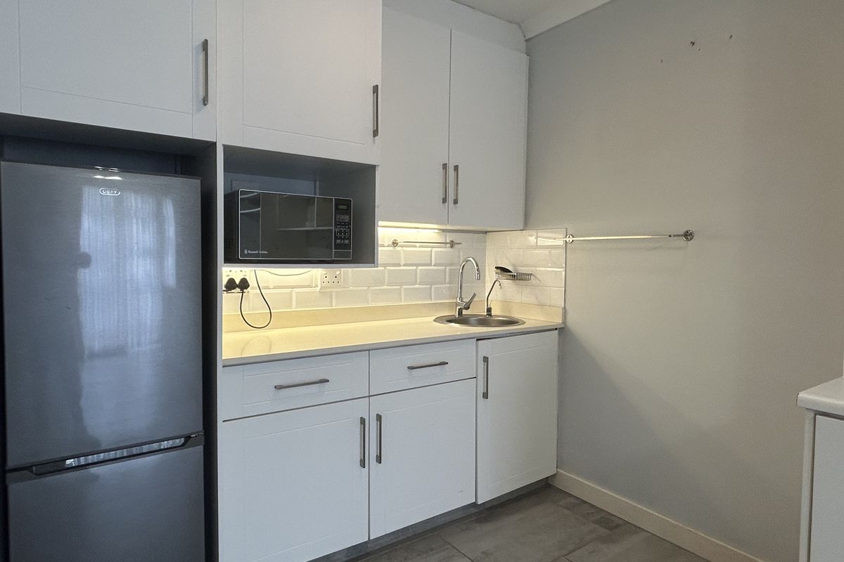 A compact, modern kitchen featuring white cabinetry, subway tile backsplash, stone countertops, and integrated microwave, presenting a clean and functional workspace.