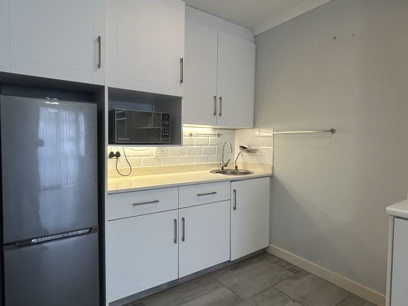 A compact, modern kitchen featuring white cabinetry, subway tile backsplash, stone countertops, and integrated microwave, presenting a clean and functional workspace.