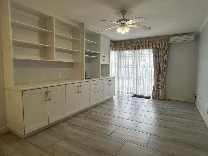 Spacious living area featuring extensive built-in cabinetry, modern tiled flooring, a ceiling fan, and split-system air conditioning with access to an outdoor area.