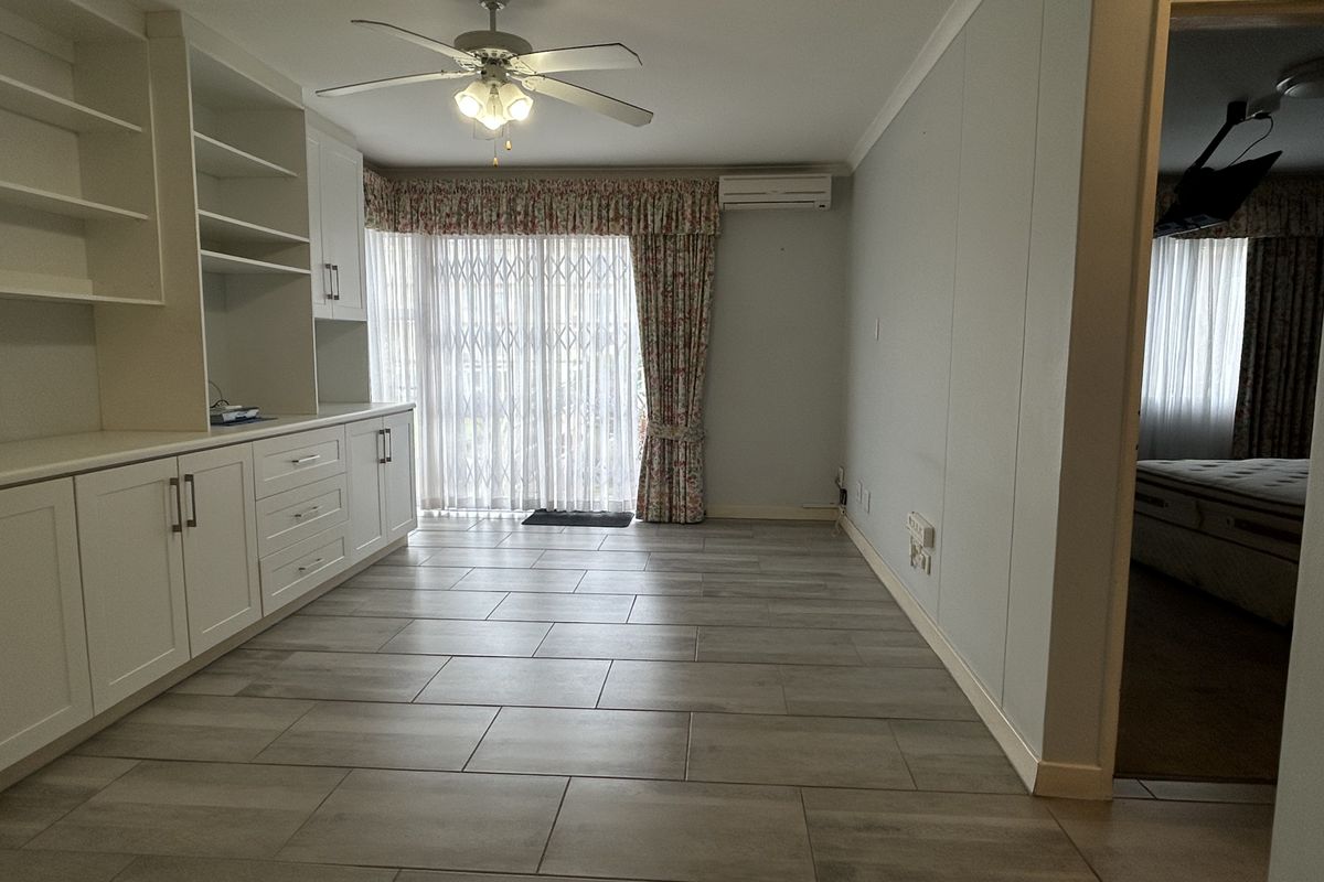A bright, open-plan living area featuring modern tiled flooring, extensive built-in cabinetry, a ceiling fan, and a split-system air conditioner with access to the outdoors.