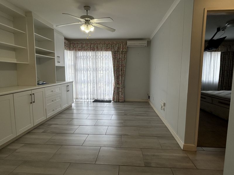 A bright, open-plan living area featuring modern tiled flooring, extensive built-in cabinetry, a ceiling fan, and a split-system air conditioner with access to the outdoors.