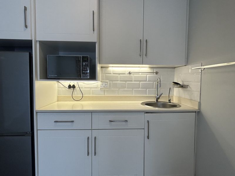 A compact, well-maintained kitchen area featuring white cabinetry, subway tile backsplash, stone countertops, and integrated under-cabinet lighting.