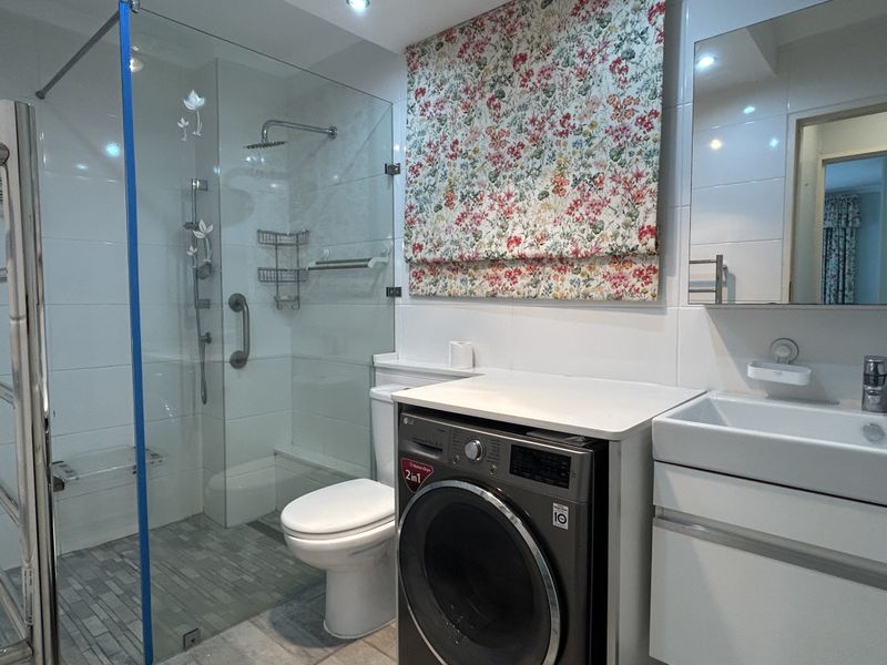 Modern bathroom featuring a glass-enclosed walk-in shower, vanity basin, and integrated laundry space with clean white tiling and contemporary fixtures.