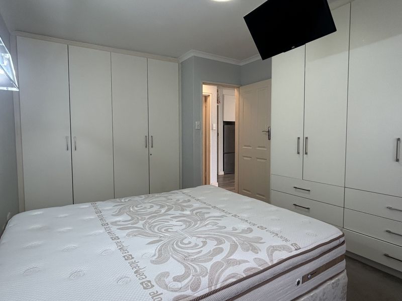 A bedroom featuring extensive built-in wardrobe storage with a neutral finish and access to an adjoining room.