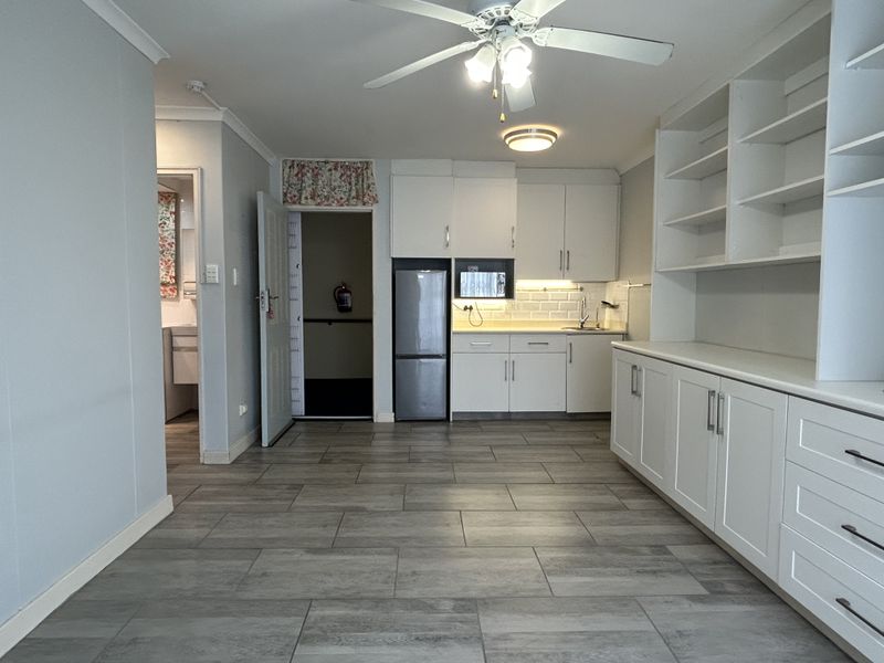 An open-plan living and kitchen area featuring modern tiled flooring, white built-in cabinetry, ample shelving, and a ceiling fan in a well-maintained retirement unit.
