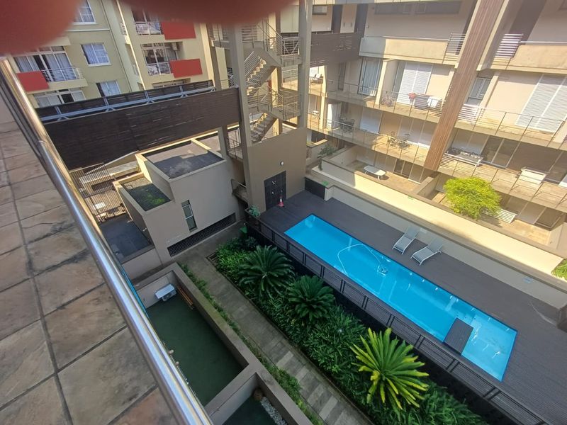 Elevated view of the apartment complex courtyard featuring a swimming pool, wooden decking, landscaped garden areas, and external staircases.