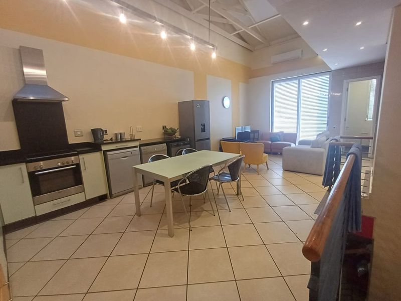 Spacious open-plan living and kitchen area featuring tiled floors, built-in oven with extractor, and access to a balcony through sliding glass doors.