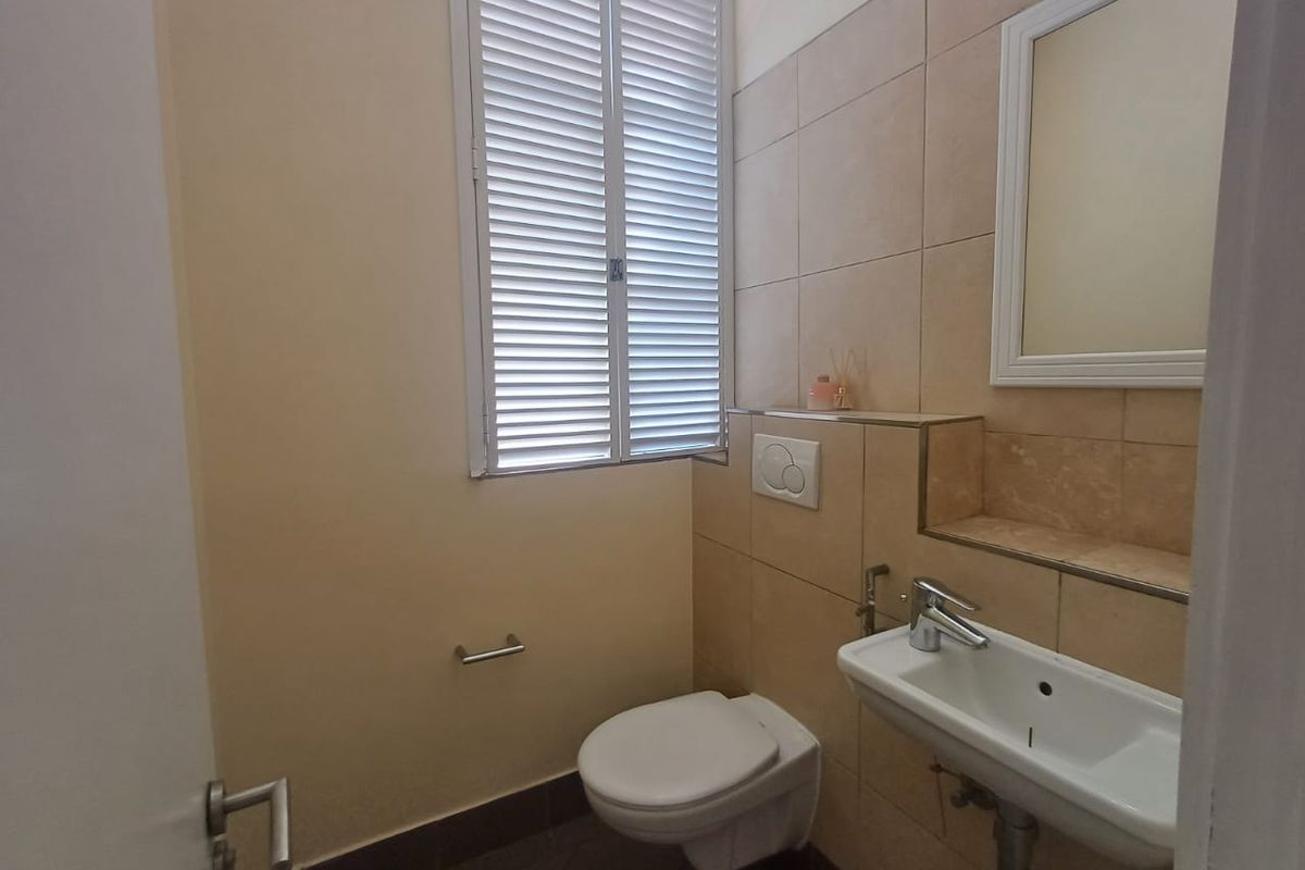 A clean and functional guest bathroom featuring a wall-mounted toilet, basin, and tiled wall finishes with a shuttered window.